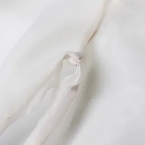 Close-up of the delicate white translucent fabric and elegant knot detail of the blouse