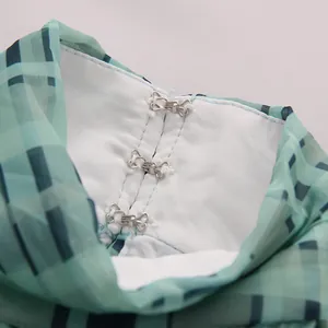 Detailaufnahme des Haken- und Ösenverschlusses an einer grünen Karochiffonbluse