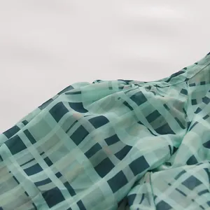Nahaufnahme einer grün karierten Chiffonbluse, die Stofftextur und feine Nähte zeigt