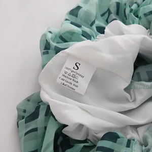 Nahaufnahme des Pflegeetiketts einer grünen Chiffonbluse, 100 % Polyester-Material