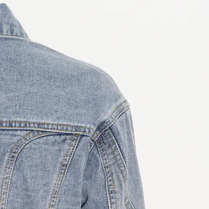 Detailaufnahme der Schulter einer hellblauen Jeansjacke mit gelben Ziernähten und Denim-Textur.