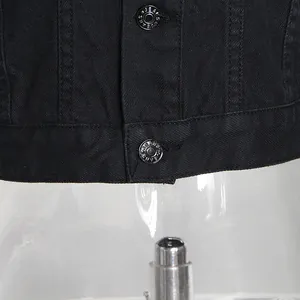 Nahaufnahme eines schwarzen Jeansjackensaums für Damen mit geprägten Metallknöpfen.