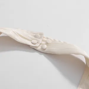 Detailed macro view of elegant cream fabric buttons on a pleated halter neck top