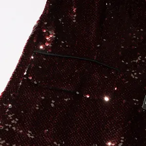 Detail of a burgundy sequined blazer showing glittery fabric and a black trimmed pocket.