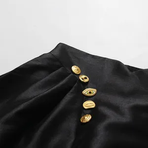 Detailansicht kunstvoller Goldknöpfe in Augen- und Lippenform an einem schwarzen Faltenrock.
