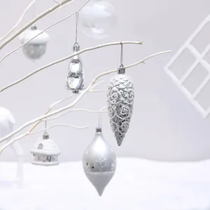 Set of silver and white Christmas tree ornaments in diverse shapes on white branches.