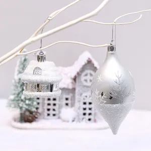 Silver and white Christmas ornaments hanging on branches with snowy house background