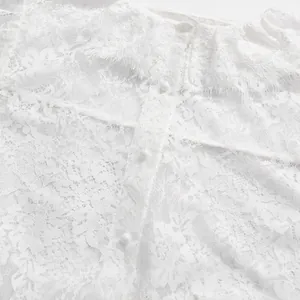 Dettaglio del tessuto in pizzo ricamato bianco e piccoli bottoni su una camicetta stile francese.