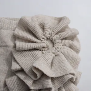 Close-up detail of a decorative 3D ruffled flower on a beige ribbed knit garment