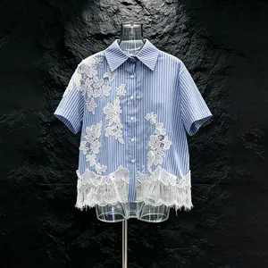 Dettaglio di una camicia a righe blu con applicazioni in pizzo bianco e orlo con frange.