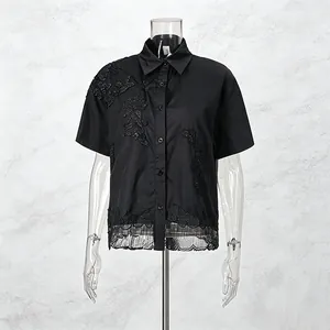 Dettaglio di camicia nera a maniche corte con ricamo floreale e bordo traforato.