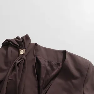 Close-up of deep V-neck blazer with decorative drape and gold metal buckle.