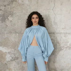 Model draagt een lichtblauwe cape blouse met pofmouwen en bijpassende broek bij een muur