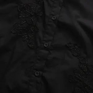 Dettaglio di una camicia nera a maniche corte con patchwork in pizzo e bottoni neri