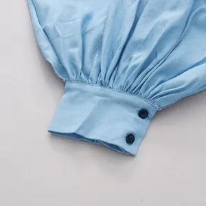 Detail van een lichtblauwe pofmouw blouse met een manchet met knopen en geplooide stof.