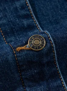 Nahaufnahme der Vintage-Bronzeknopf-Details und gelben Nähte an der blauen Jeansjacke