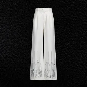 Detailed view of silver sequin patterns on white high-waisted straight trousers.