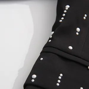 Detailed close-up of white pearl decorations on black premium blazer jacket fabric.