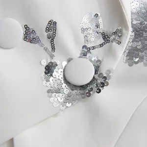 Detail of silver sequin embroidery and fabric buttons on a white notched lapel blazer