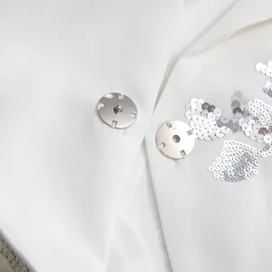 Detailed view of silver snap button and sequin floral embroidery on white lapel top