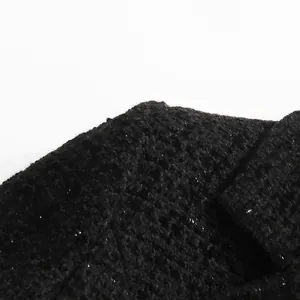 Detailed macro view showing the textured black bouclé tweed fabric of a lady garment
