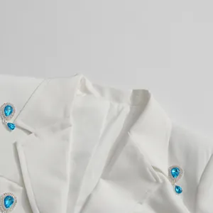 Close-up detail showing the blue teardrop rhinestone embellishments on white blazer