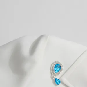 Close-up of a sparkling blue teardrop brooch on a white minimalist blazer lapel