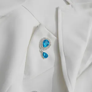 Detailed macro shot of a blue teardrop crystal brooch on a white suit jacket