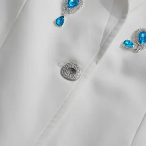 Close-up detail of silver textured button and blue teardrop rhinestones on white blazer