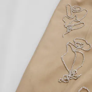 Dettaglio ricamo rosa con strass su elegante tessuto beige per completo da donna.