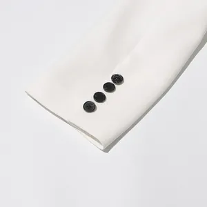 Close-up detail of white blazer sleeve cuff with decorative black buttons and smooth fabric.