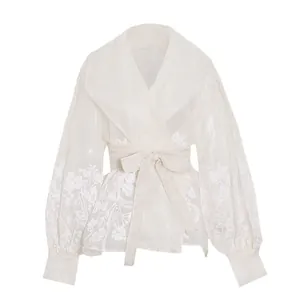 Macro detail view of elegant white organza blouse with floral embroidery and waist tie