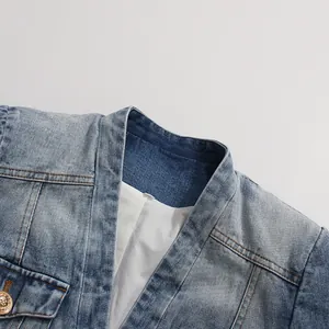 Close-up of a light wash denim blazer featuring a gold lion head button detail