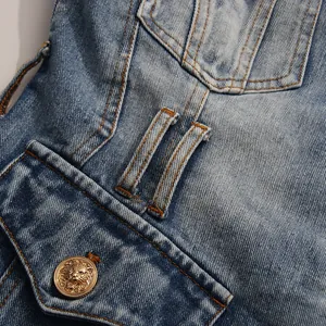 Macro view of a distressed blue denim blazer featuring a golden lion head button.