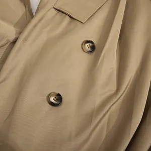 Primer plano de botones de carey y tejido de sarga caqui en un vestido de doble botonadura.