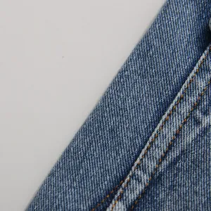 Macro detail of blue denim fabric with orange double stitching on vintage wash jacket.