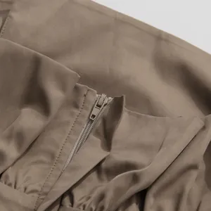 Close-up view of the high-quality zipper and pleated waist detail on a khaki jumpsuit.