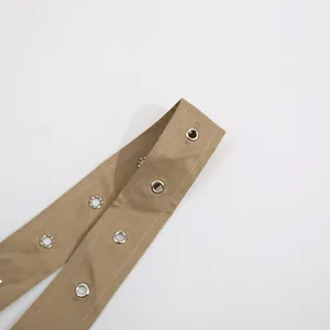 Detalle de correa de tela caqui con ojales metálicos plateados para un vestido con lazo