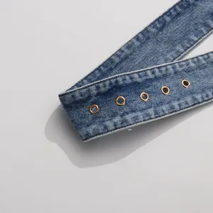 Close-up of washed denim strap with gold eyelets for women's denim blazer jacket.