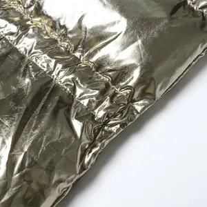 Detailweergave van glanzende goudkleurige metallic stof met doorgestikte textuur op vest