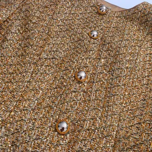 Close-up view of elegant golden tweed fabric with sequins and polished silver buttons