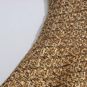 Close-up view of premium golden tweed fabric with intricate sequin details and texture.