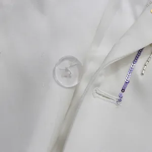 Detailed macro view of elegant white blazer featuring purple sequins and a clear resin button