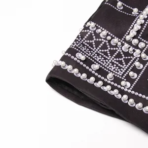 Detailed macro shot of white pearls and geometric printing on a black court-style jacket.