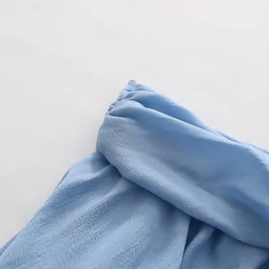 Close-up detail of a light blue off-shoulder top featuring fine pleated neckline texture