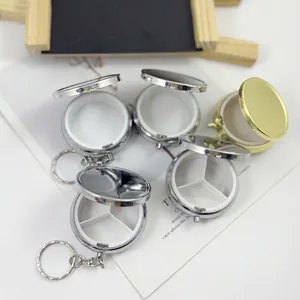 Detail van ronde metalen pillendoosjes met sleutelhanger, vakjes en zilver-gouden afwerking