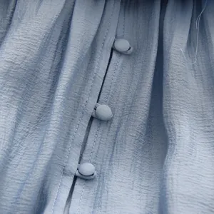 Close-up detail of fabric-covered buttons on a light blue pleated off-the-shoulder top