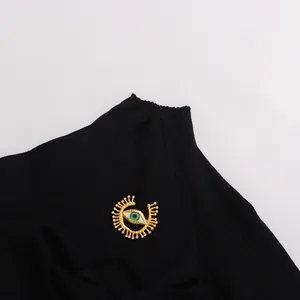 Détail d'un haut en maille côtelée noire avec un embellissement métallique en forme d'œil