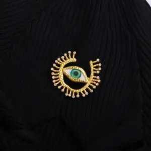 Broche œil grec doré avec émail vert et cristaux sur un vêtement en maille noire