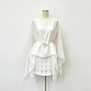 Dettaglio di camicetta in chiffon bianco stile francese con fiocco in vita e mantella.